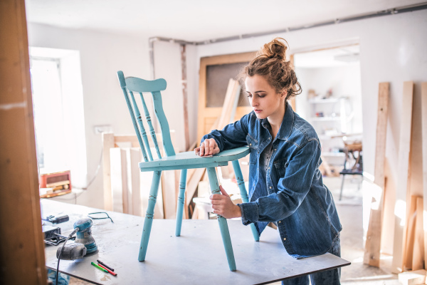 Small business of a young woman. Beautiful young woman worker in carpenter workroom. Old furniture restoration.