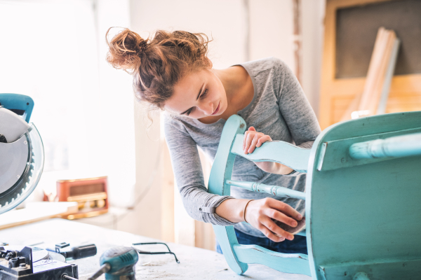 Small business of a young woman. Beautiful young woman worker in carpenter workroom. Old furniture restoration.