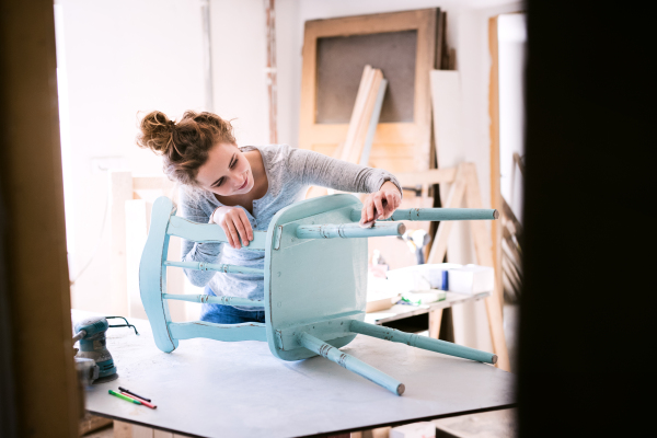 Small business of a young woman. Beautiful young woman worker in carpenter workroom. Old furniture restoration.