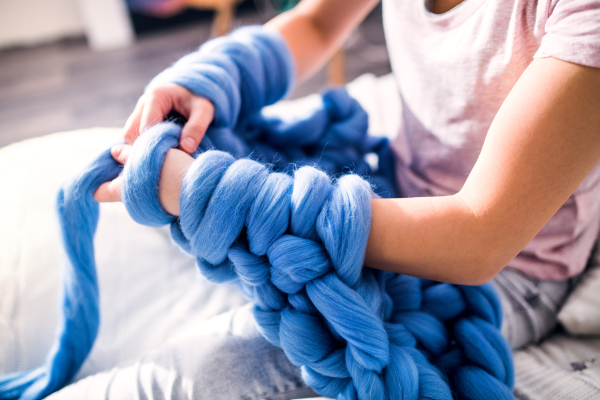 Small business of a young woman. Unrecognizable woman hand-knitting a woollen blanket.