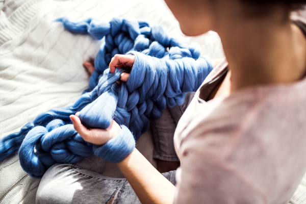 Small business of a young woman. Unrecognizable woman hand knitting a woollen blanket.