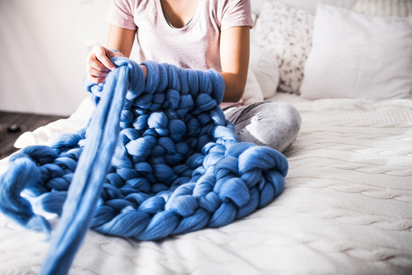 Small business of a young woman. Unrecognizable young woman hand-knitting a woollen blanket.