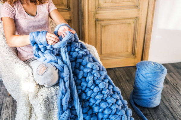 Small business of a young woman. Unrecognizable woman hand-knitting a woollen blanket.