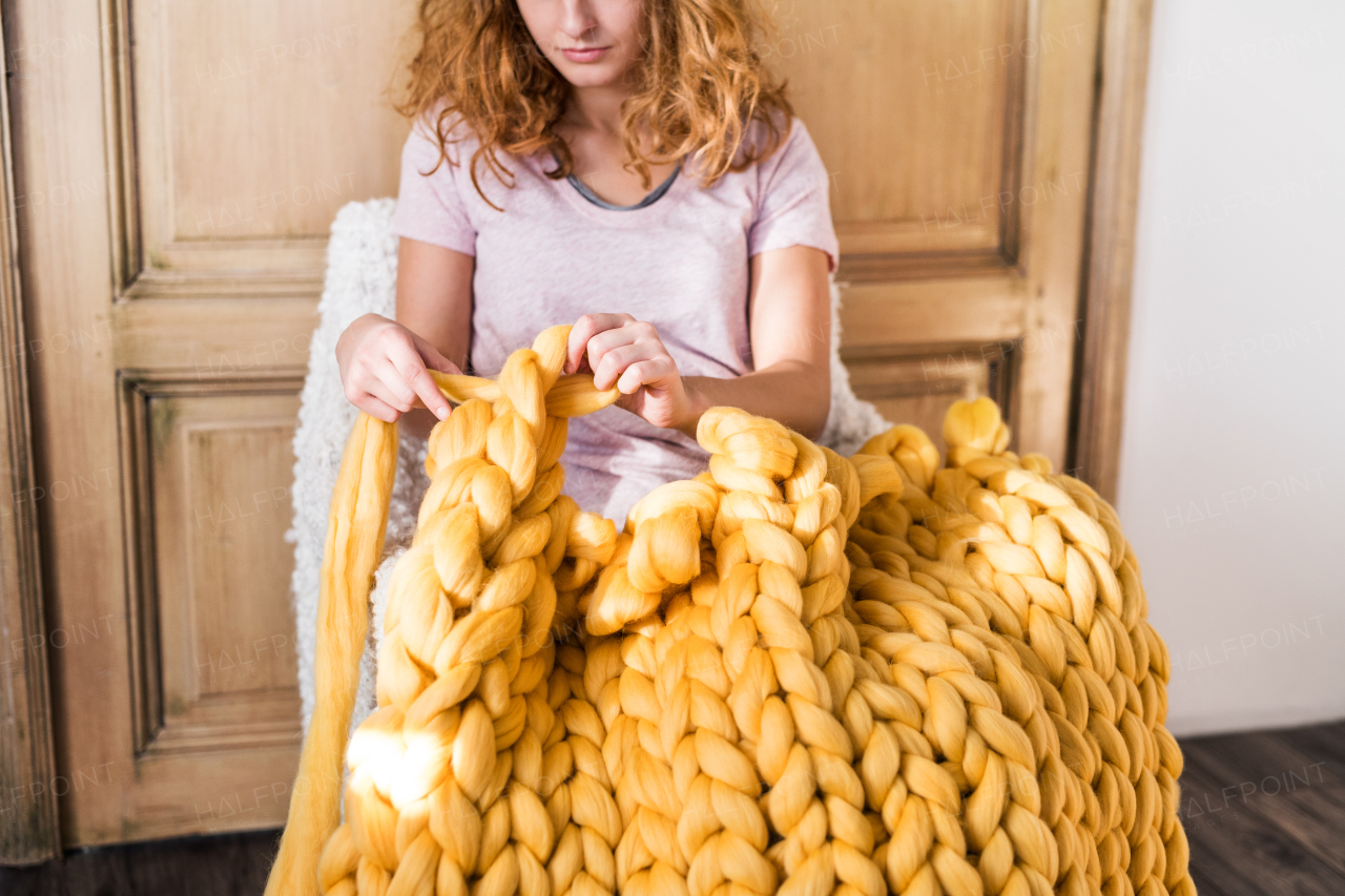 Small business of a young woman. Unrecognizable young woman hand-knitting a woollen blanket.