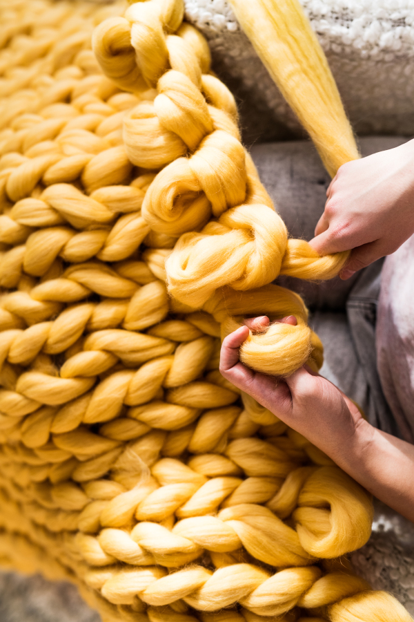 Small business of a young woman. Unrecognizable young woman hand-knitting a woollen blanket.