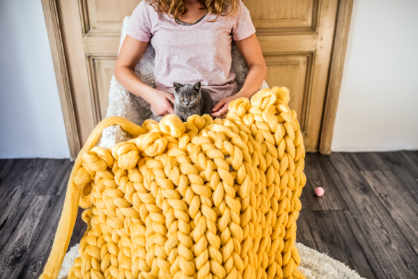 Small business of a young woman. Unrecognizable young woman with a kitten hand-knitting a woollen blanket.