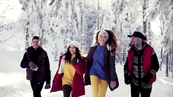 A group of cheerful young cheerful friends on a walk outdoors in snow in winter forest, running. Slow motion.