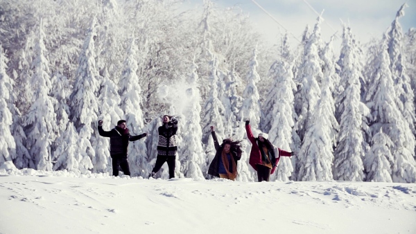 A group of young cheerful friends on a walk outdoors in snow in winter forest, having fun. Slow motion.