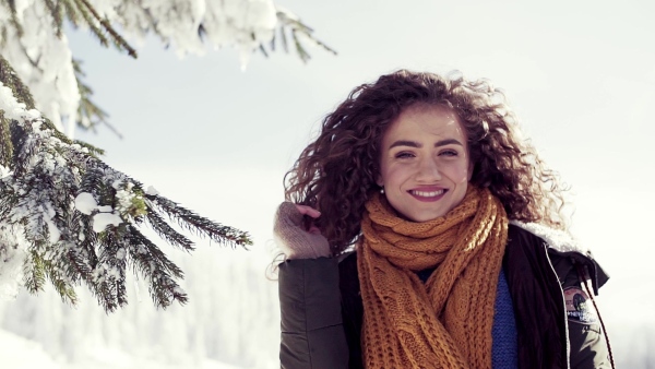 A front view portrait of young woman standing outdoors in snowy winter forest. Slow motion.