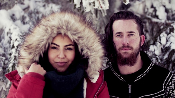 A portrait of couple standing outdoors in snow in winter forest, looking at camera. Slow motion.