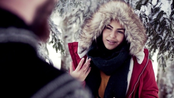 A portrait of couple standing outdoors in snow in winter forest, talking. Slow motion.