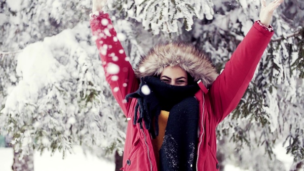 A front view portrait of young woman standing outdoors in snowy winter forest, throwing snow. Slow motion.