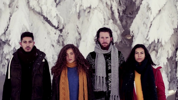 A group of young cheerful friends standing outdoors in snow in winter forest, looking at camera. Slow motion.