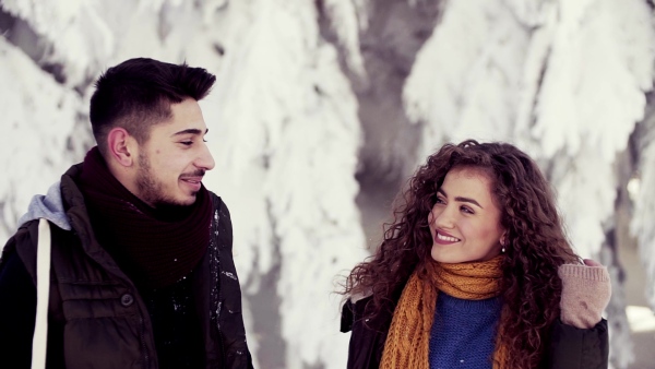 A portrait of couple standing outdoors in snow in winter forest, talking. Slow motion.