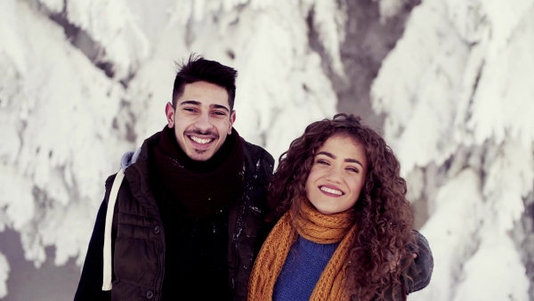 A portrait of couple standing outdoors in snow in winter forest, looking at camera. Slow motion.