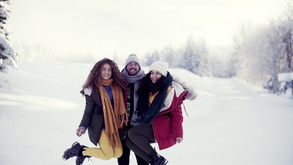 A group of cheerful young cheerful friends standing outdoors in snow in winter forest, having fun. Slow motion.