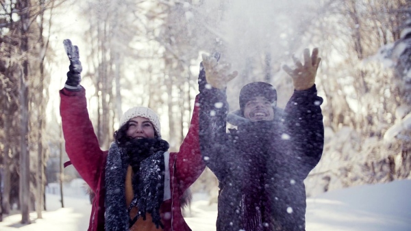 A portrait of couple standing outdoors in snow in winter forest, throwing snow. Slow motion.