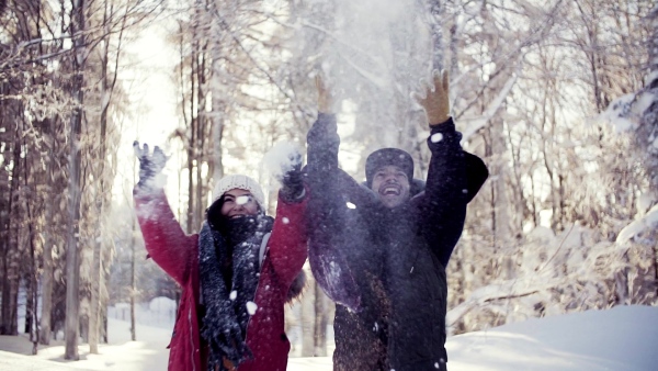 A portrait of couple standing outdoors in snow in winter forest, throwing snow. Slow motion.