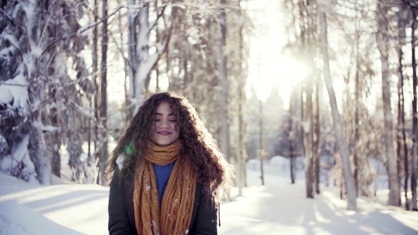 A front view portrait of young woman standing outdoors in snowy winter forest. Slow motion.