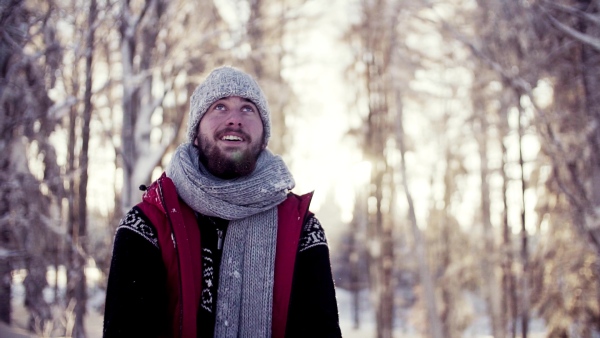 Happy young man standing outdoors in snow in winter forest, throwing snow. Slow motion.