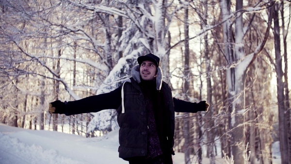 Happy young man walking outdoors in snow in winter forest. Slow motion.