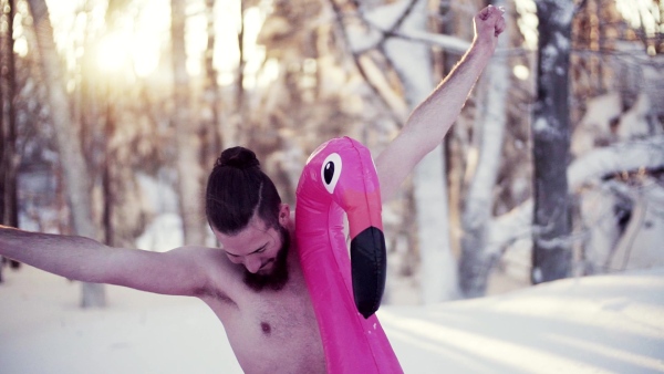 A portrait of topless young man outdoors in snow in winter forest, having fun. Slow motion.