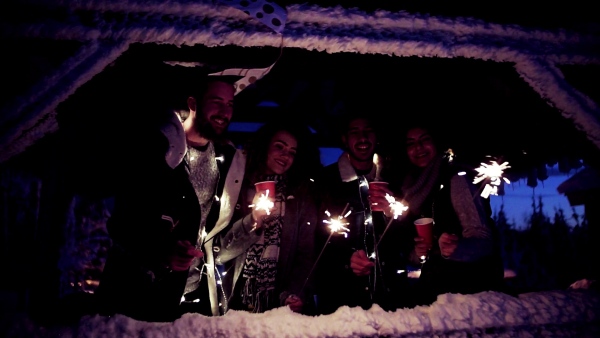 A group of young friends outdoors in snow in winter at night, holding sparklers. Slow motion.