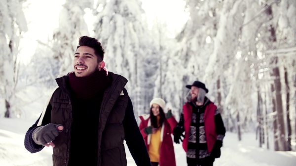 A group of young cheerful friends on a walk outdoors in snow in winter forest. Slow motion.