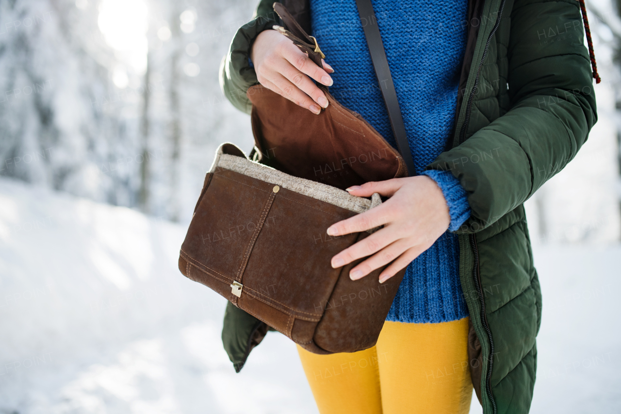 Midsection of woman with leather handbag standing outdoors in snowy winter forest.