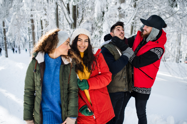 A group of young cheerful friends on a walk outdoors in snow in winter forest, having fun.