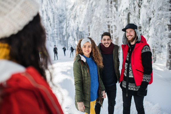 A group of young cheerful friends on a walk outdoors in snow in winter, talking.