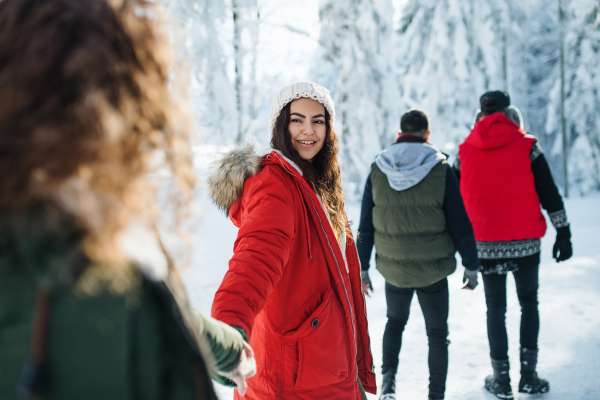 A group of young friends on a walk outdoors in snow in winter forest, walking.