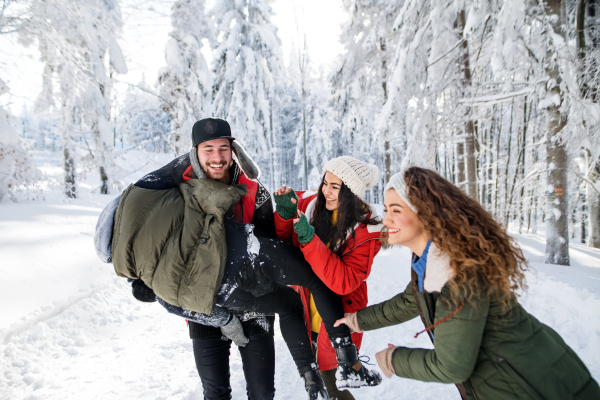 A group of young cheerful friends on a walk outdoors in snow in winter forest, having fun.