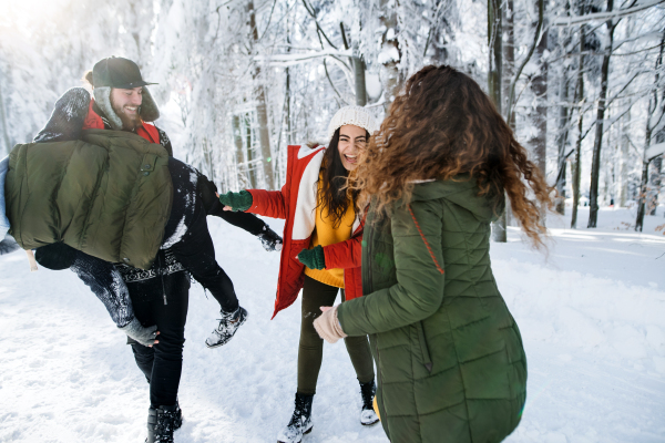 A group of young cheerful friends on a walk outdoors in snow in winter forest, having fun.