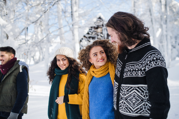 A group of young cheerful friends on a walk outdoors in snow in winter, talking.