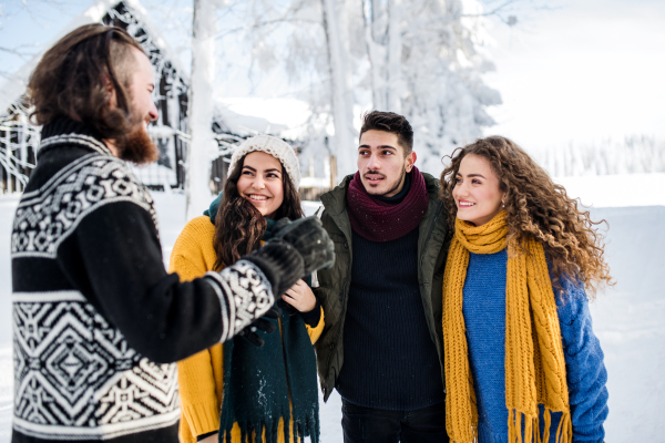 A group of young cheerful friends on a walk outdoors in snow in winter, talking.