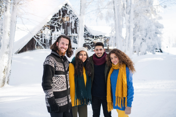 A group of young cheerful friends on a walk outdoors in snow in winter, looking at camera.