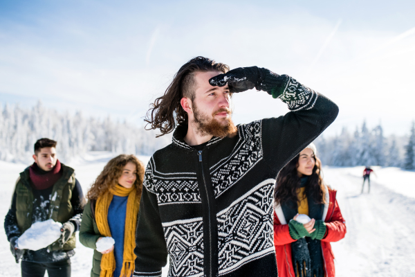 A group of young cheerful friends on a walk outdoors in snow in winter forest, having fun.