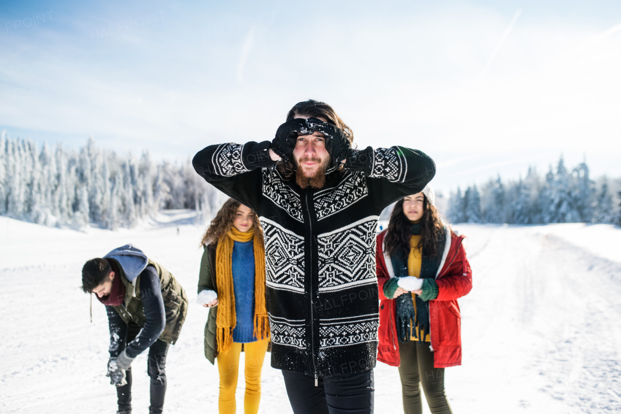 A group of young cheerful friends on a walk outdoors in snow in winter forest, walking.