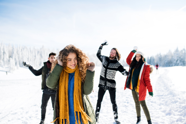 A group of young cheerful friends on a walk outdoors in snow in winter forest, having fun.