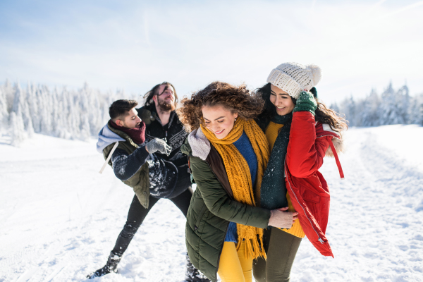 A group of young cheerful friends on a walk outdoors in snow in winter forest, having fun.