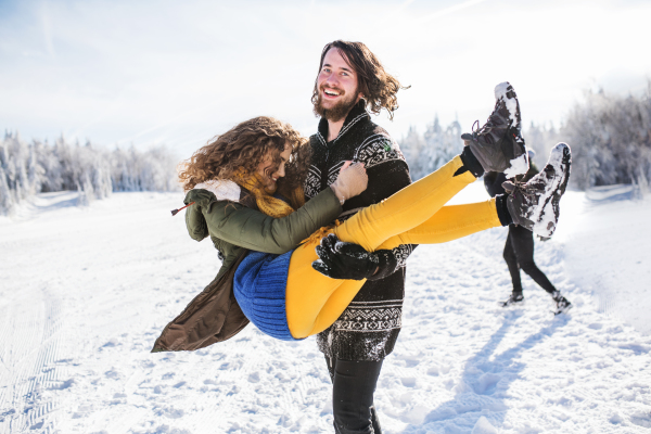 A group of young cheerful friends on a walk outdoors in snow in winter forest, having fun.