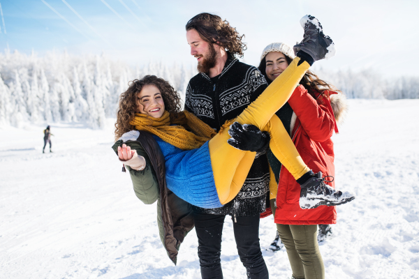 A group of young cheerful friends on a walk outdoors in snow in winter forest, having fun.