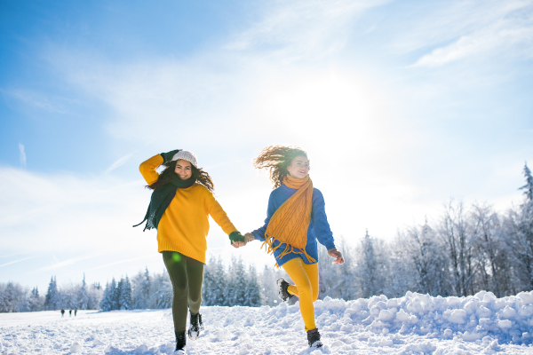 Front view of young cheerful friends on a walk outdoors in snow in winter, running.