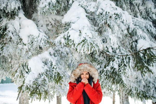 A front view portrait of young woman standing outdoors in snowy winter forest, wearing fur hood.