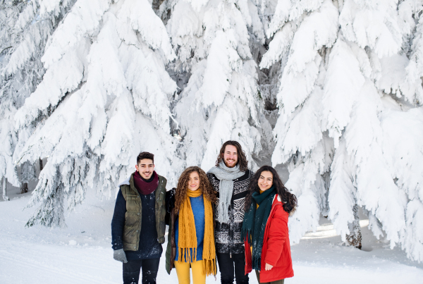 A group of young cheerful friends on a walk outdoors in snow in winter, looking at camera.