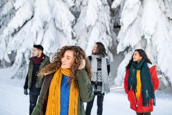 A group of young cheerful friends on a walk outdoors in snow in winter forest, walking.