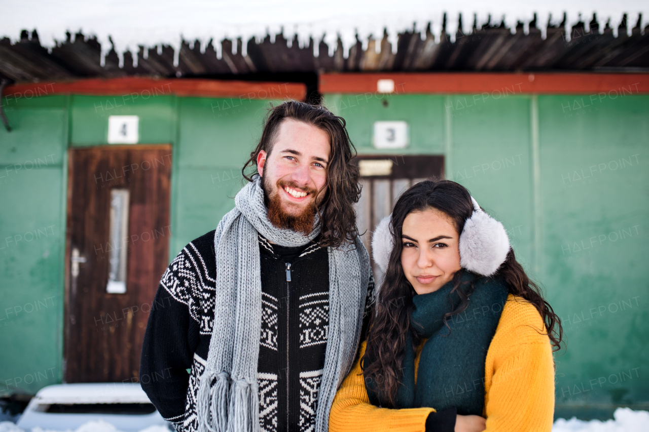 A portrait of young couple standing outdoors in winter, looking at camera.