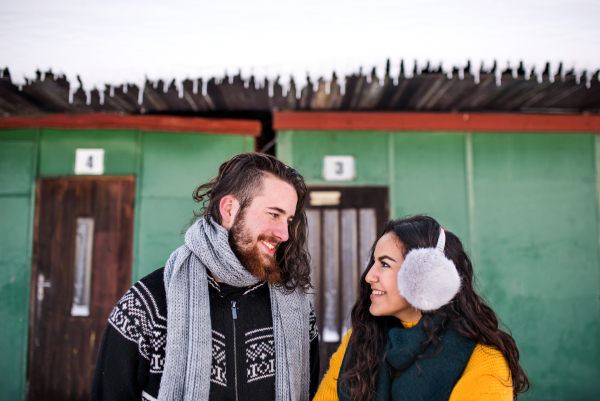 A portrait of young couple standing outdoors in winter, talking.