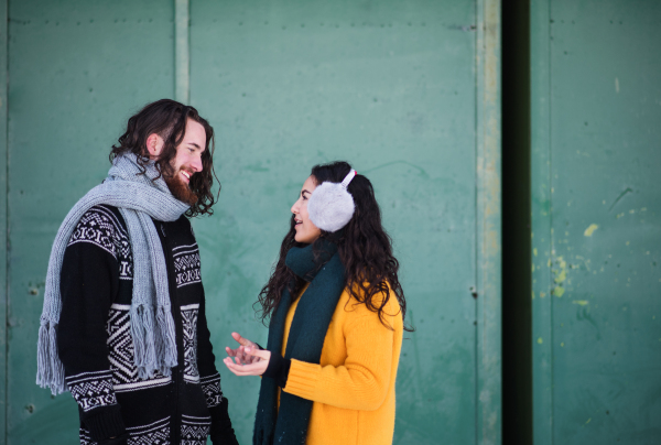 A side view portrait of young couple standing outdoors in winter, talking.